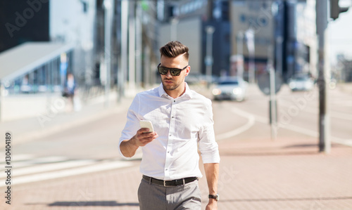 man in sunglasses with smartphone walking at city © Syda Productions