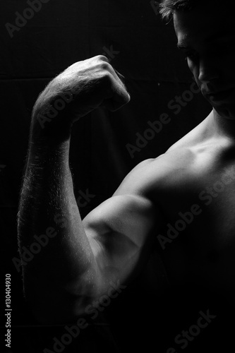 Male fitness model showing muscles in studio with a black backgr