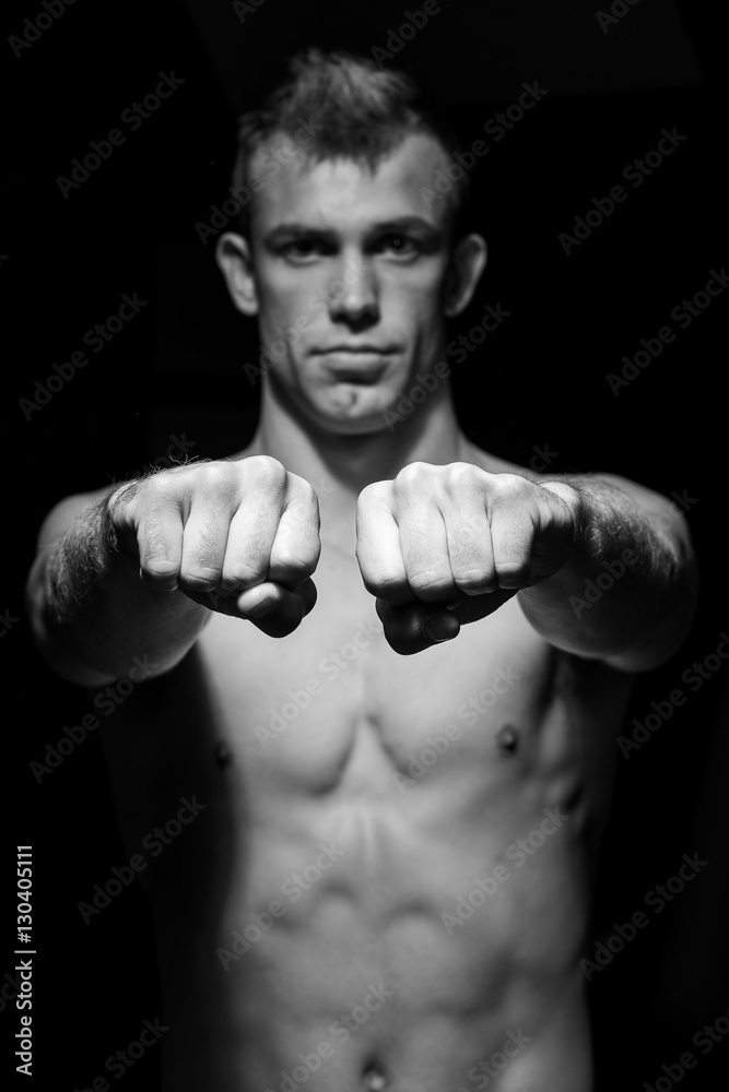Male fitness model showing muscles in studio with a black backgr Male fitness model showing muscles in studio with a black backgr