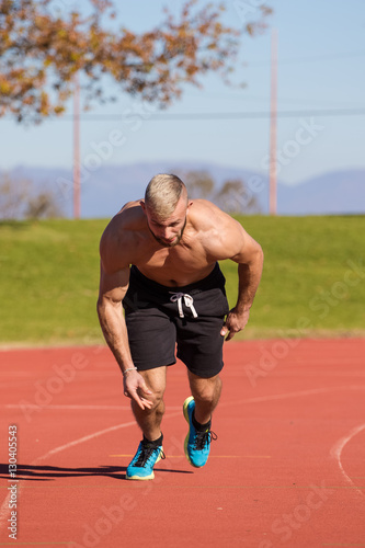 Male Athlete sprinting on a tartan athletics track on a bright s