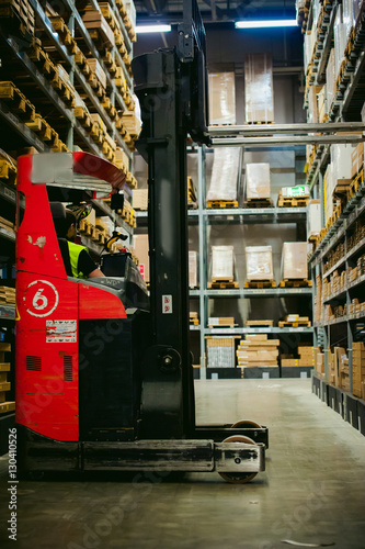 young man in working clothes, driver Reachtruck busy working on the logistics warehouse store photo