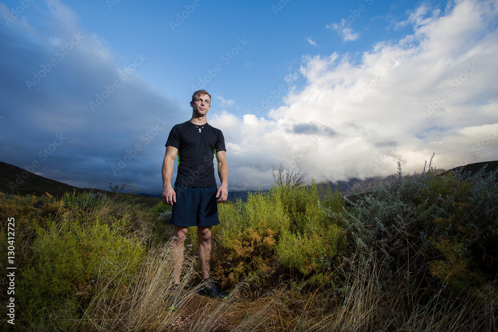 Male fitness model running allong a trail in the field, wearing