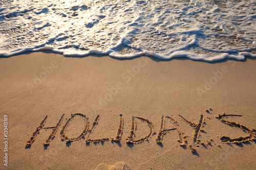 mot holidays écrit en anglais sur le sable sur la plage
