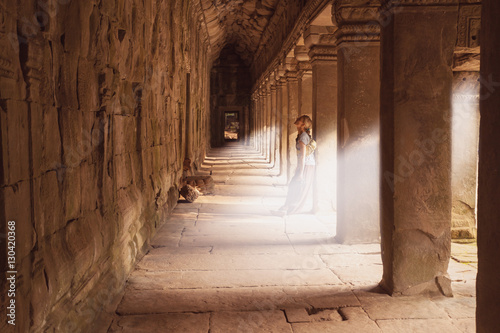 Female traveler standing in the Temple Gallery Ta - Prohm in the rays of sunlight. Angkor, Cambodia. Ancient ruins.