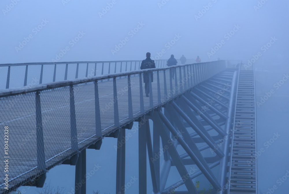 Pedestrians walking over a modern footbridge on a foggy, autumn morning in Lyon, France. Pedestrians walking over a modern footbridge on a foggy, autumn morning in Lyon, France.