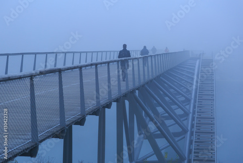 Pedestrians walking over a modern footbridge on a foggy, autumn morning in Lyon, France.