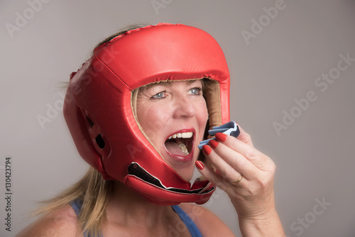 Female boxer wearing a safety head guard and inserting a gum shield into her mouth photo