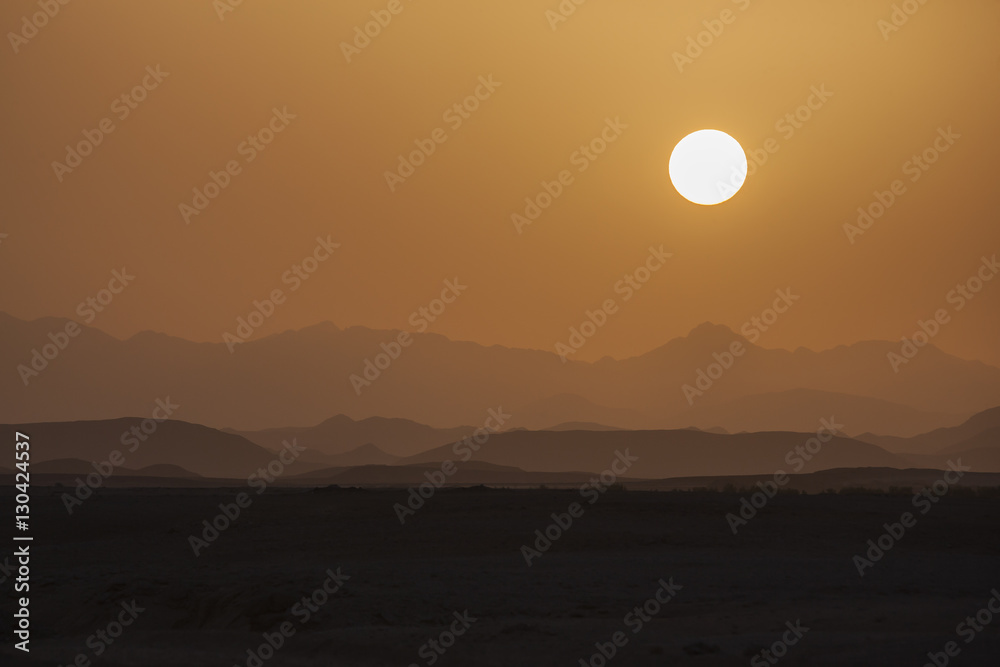 Landscape in orange palette, solar disk above hills and desert at the sunset, Egypt