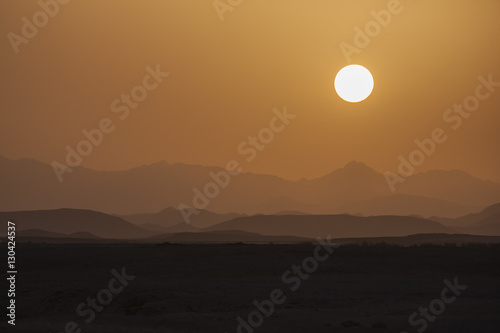 Landscape in orange palette, solar disk above hills and desert at the sunset, Egypt