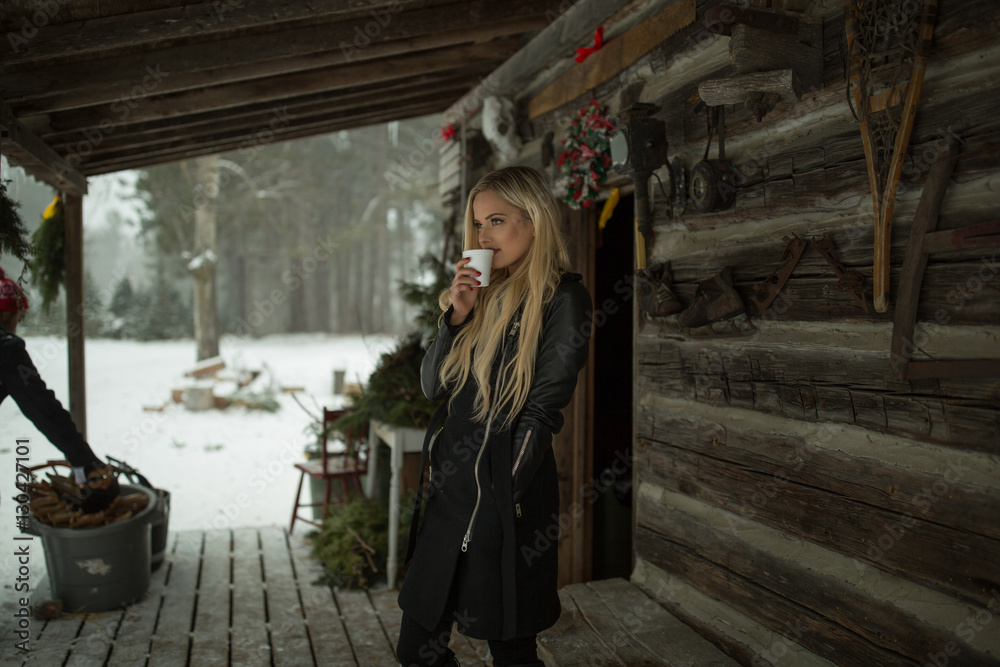 Blonde woman drinks coffee at a snowy cabin