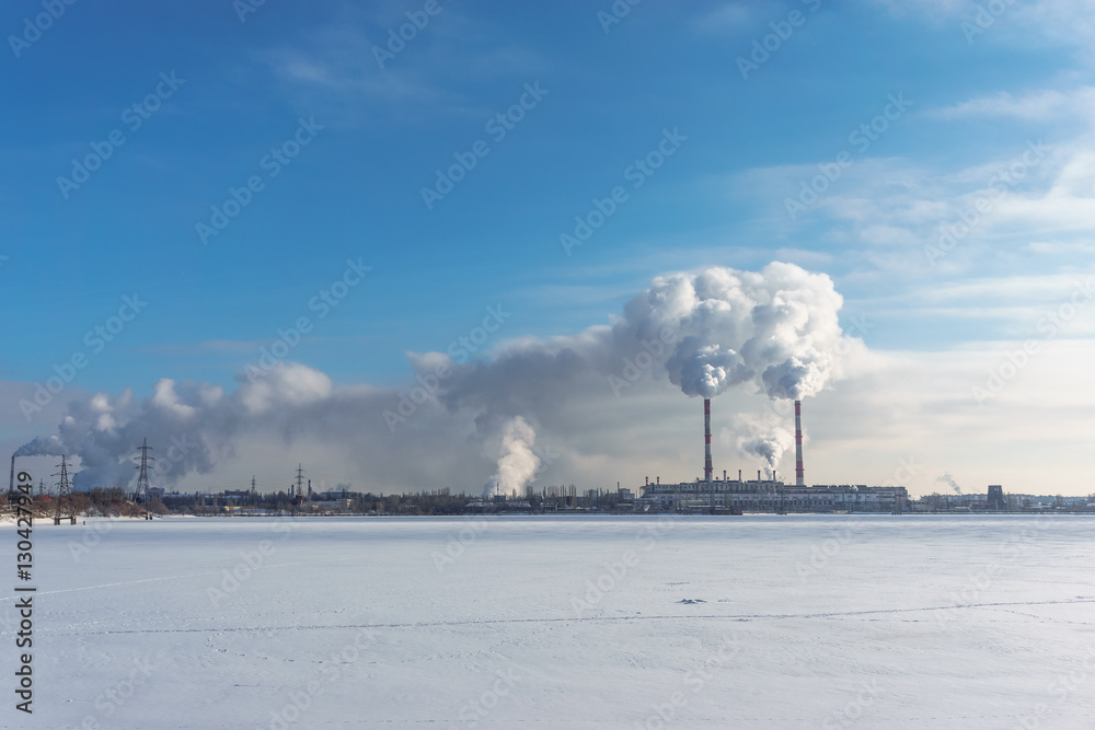 Power station with pipes of which poured smoke on a frozen river. Free copyspace