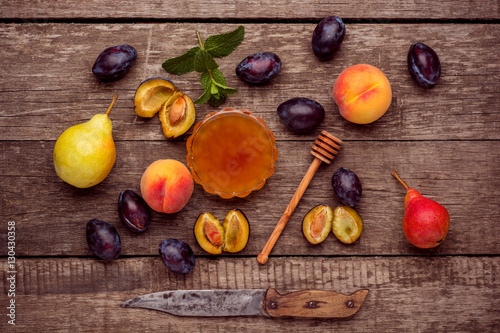 Ripe fruits of peach, plums and pear with honey in a tray on rustic background. Top view