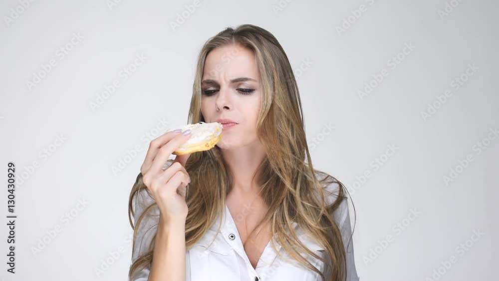 Beautiful young woman with long hair in white shirt eating donut Beautiful young woman with long hair in white shirt eating donut