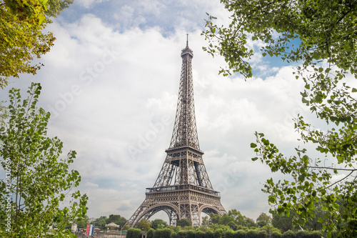 View on Eiffel tower through green trees with cloud bckground. Eiffel Tower from Champ de Mars, Paris, France.