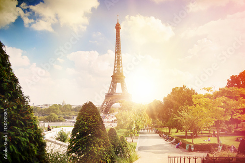 Canvas Print View on Eiffel tower through green summer trees with sunset rays