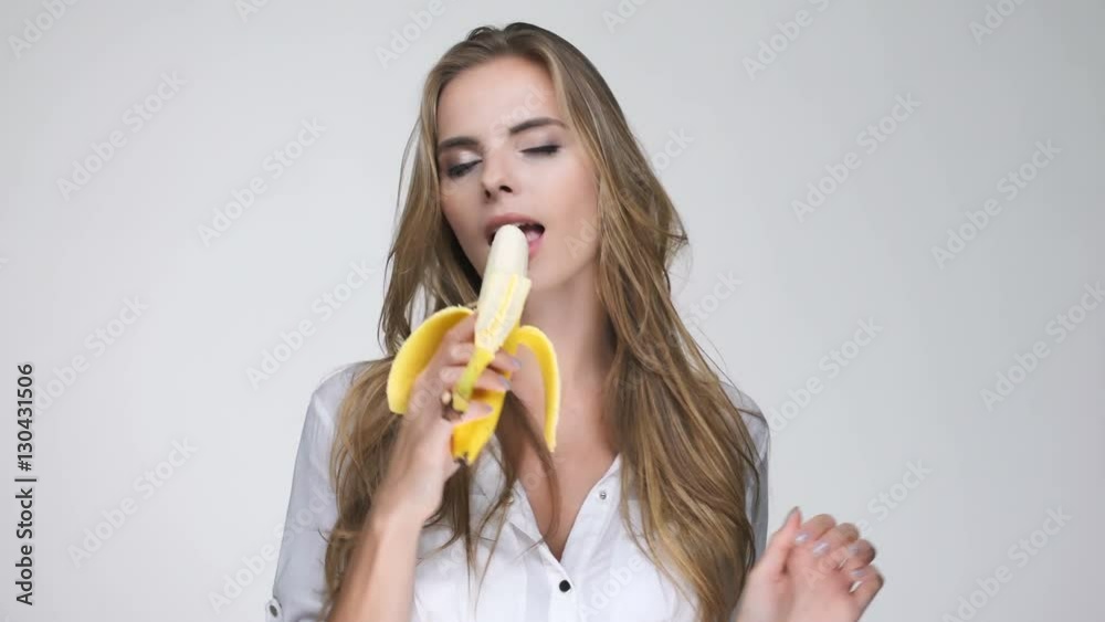Pretty young woman in white shirt eating banana