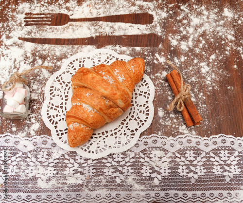 On a wooden board is a croissant with chocolate under the white cloth beside him cinnamon, various decorations, all floured. photo