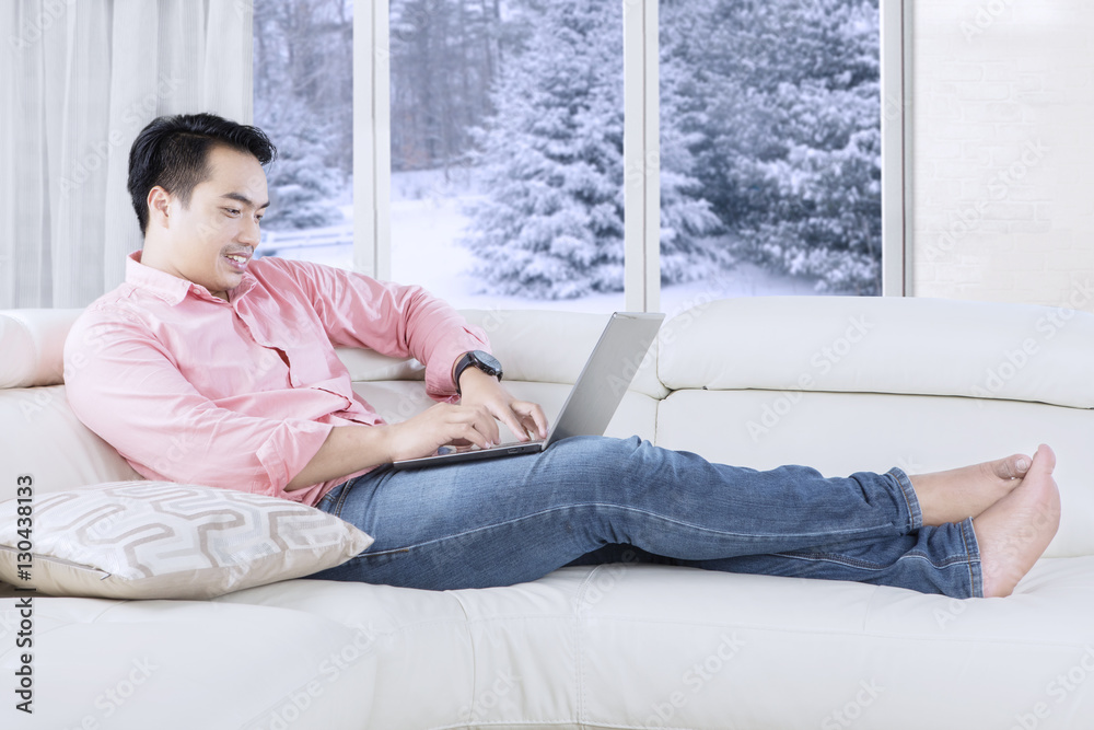 Naklejka premium Man typing with laptop on sofa