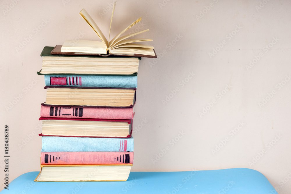 Fototapeta premium Open book, stack of colorful hardback books on light table. Back to school. Copy space for text