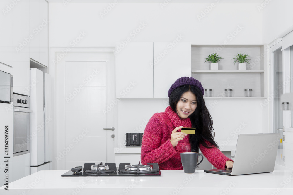Woman uses laptop and credit card in kitchen Woman uses laptop and credit card in kitchen