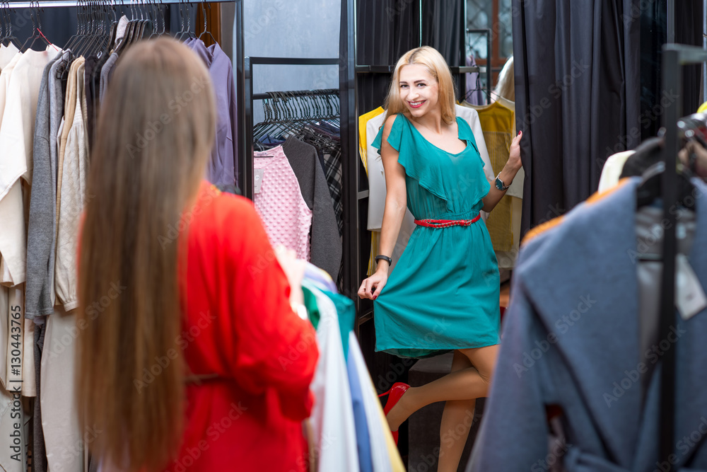 Happy woman trying a new dress in the wardrobe at the clothing store. Female friends having fun shopping clothes
