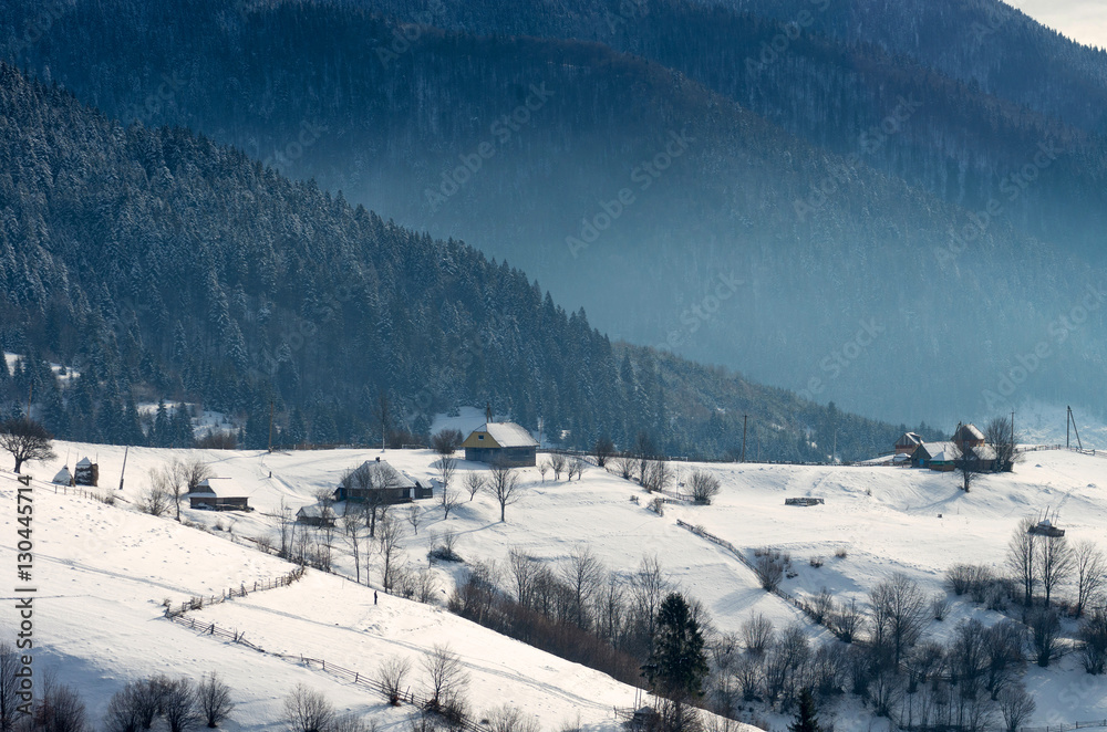 Little Farm on the edge of a winter forest. Winter mountain landscape with haze.