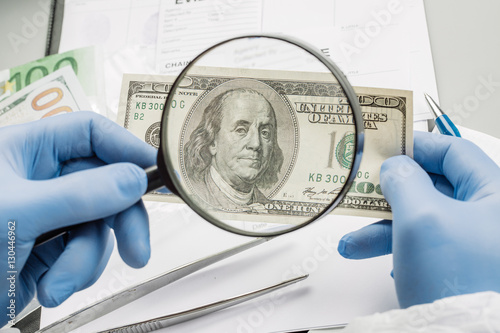 policewoman with magnifying glass checks suspicious money. photo