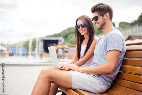 Beautiful happy couple with laptop sitting on bench and watching