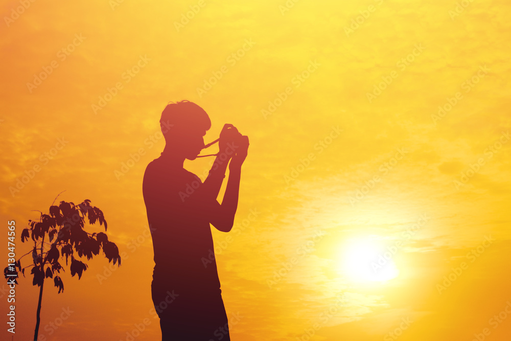 Silhouette of young photographer holding a camera on sunset.