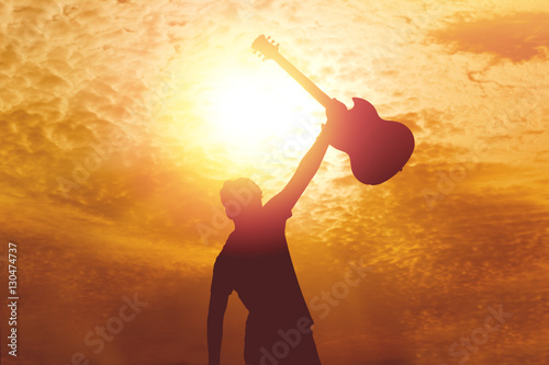 Silhouette of young musician holding a guitar on sunset.