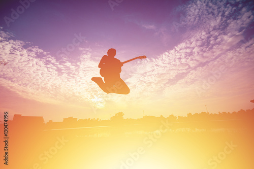 Silhouette of young musician holding a guitar on sunset.