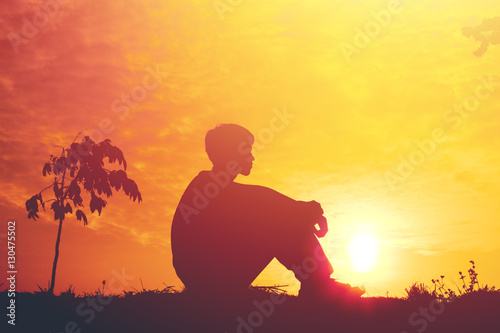 Silhouette of a young boy sitting sadly on sunset.