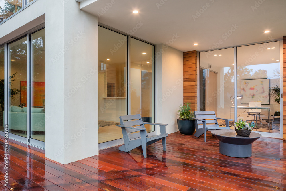 Wet wooden deck with furniture and open doors leading to inside. Stock ...