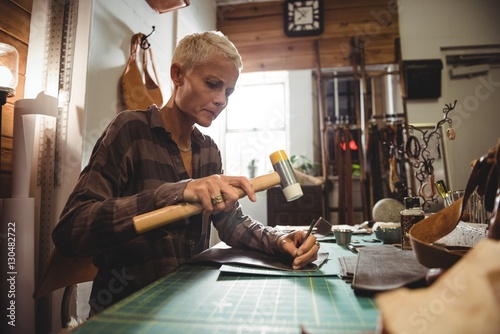 Attentive craftswoman nailing leather photo