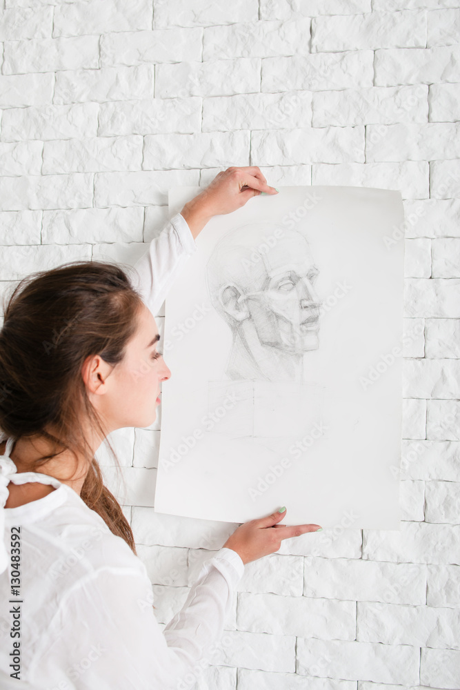 Artist hanging her pencil portrait on wall. Close-up of attractive woman decorating white brick side in her workshop with sketch. Art, creativity, hobby, talent,drawing, relax concept Artist hanging her pencil portrait on wall. Close-up of attractive woman decorating white brick side in her workshop with sketch. Art, creativity, hobby, talent,drawing, relax concept