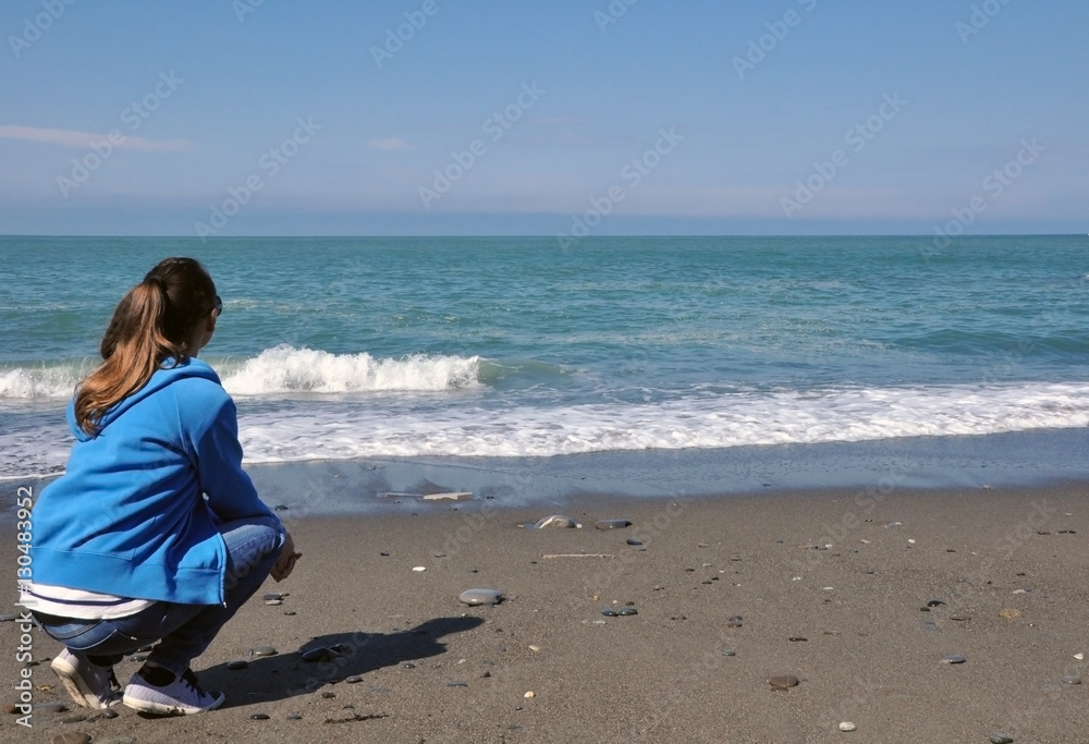 Young woman sitting on the beach looking at the sea Young woman sitting on the beach looking at the sea