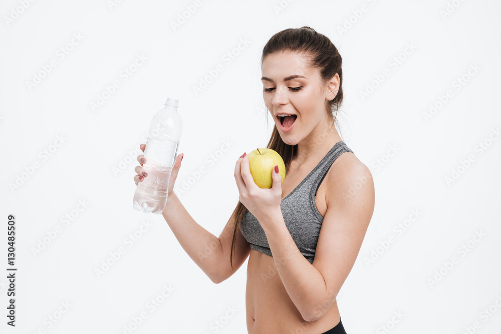 Young sports woman holding water bottle and biting apple Young sports woman holding water bottle and biting apple