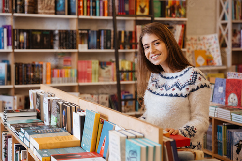 Pretty young woman choosing books in library