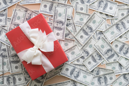 Red gift box with white ribbons on pile of dollars banknotes fla