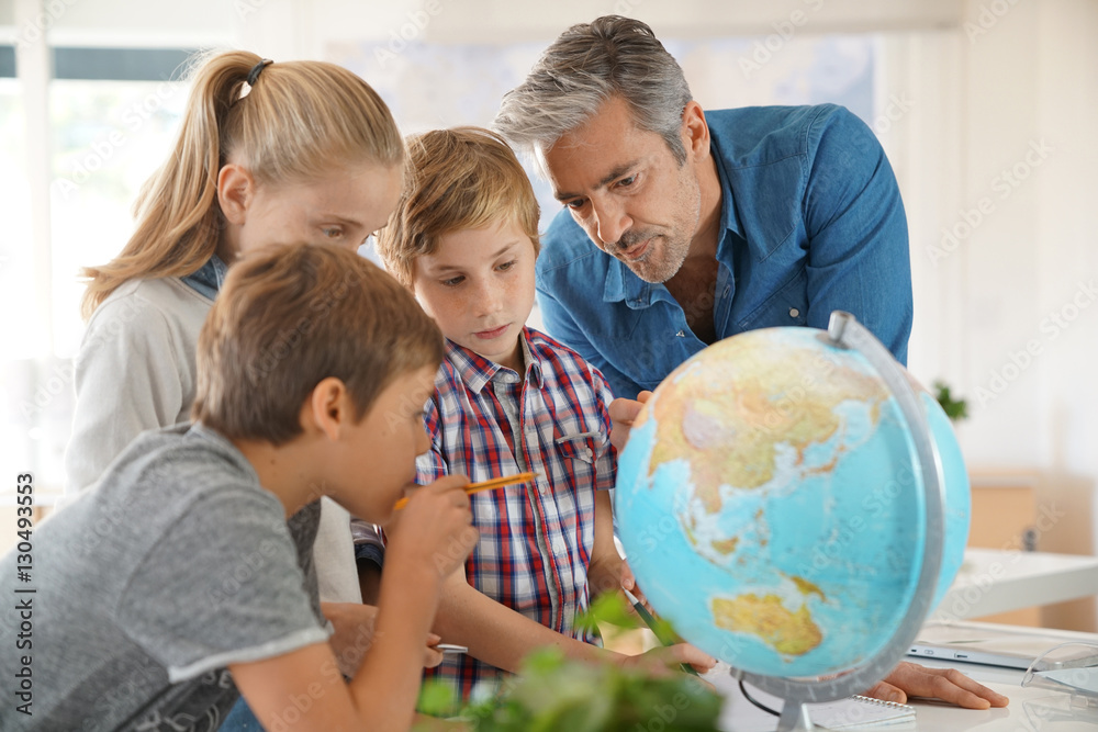 Fototapeta premium Teacher with kids in geography class looking at globe