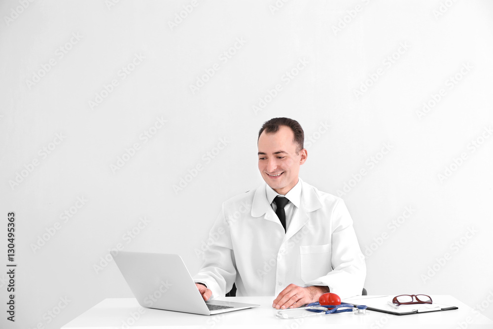 Doctor sitting at table with laptop and medical equipment on light background Doctor sitting at table with laptop and medical equipment on light background