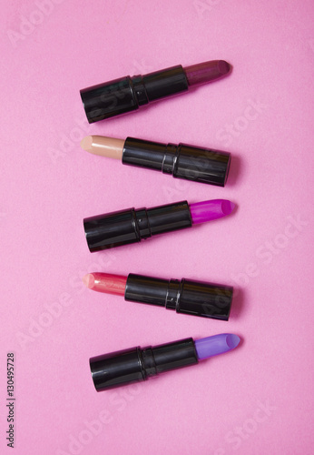 Aerial view of various color lip stick make up on a bright pink background
