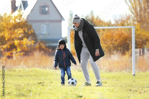 Father and son playing football on soccer pitch