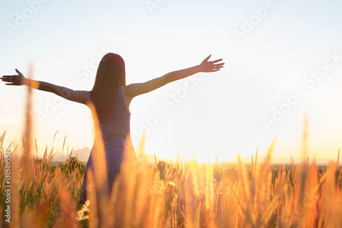Trendy girl in stylish summer dress with beautiful hat walking in the field with flowers in sunlight