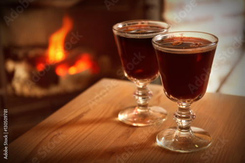 Glasses of mulled wine on wooden table against blurred fireplace