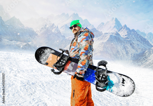 Snowboarder carries a board in the hands. Evening snowfall in the mountains.