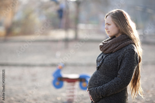Junge Frau mit Babybauch in herbstlicher Spielplatzszenerie
