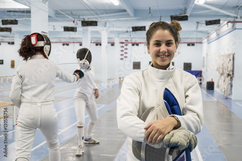 Smiling female fencer with fencing match in the background