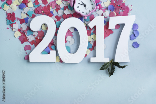 Overhead view of happy new year 2017 number and alarma clock five minute before midnight on scattered colorful party confetti background.