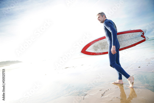 Surfer on the beach holding surfboard, getting in the water